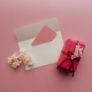 Top-down shot of a wrapped pink gift and envelope with flowers on a pink background.